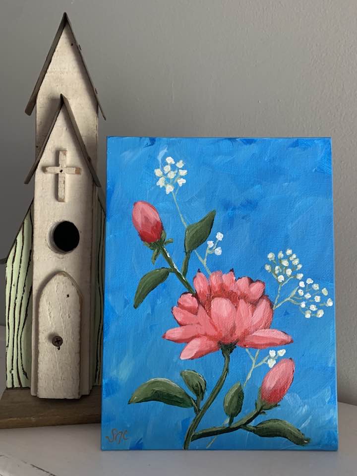 A painting with blue background, red roses and baby's breath sitting next to a birdhouse.